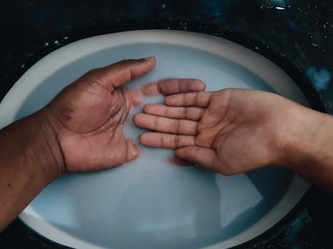 Close-up of two diverse hands submerged in a basin, highlighting unity and diversity.